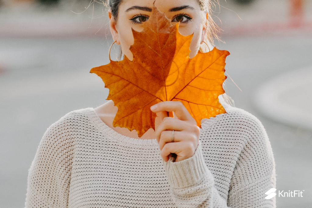 A woman who has recently enjoyed knitting the unshaped sweater wears a cream-colored boxy garment and holds a maple leave over her face